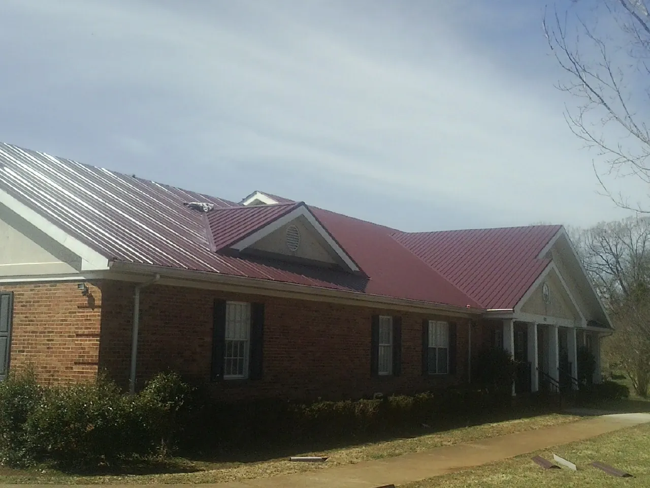 Red metal roof with gabled entries on a long brick building, from a Hail Damage Roof Repair job in Milpitas